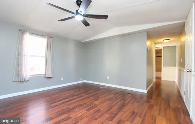 an empty room with wooden floor a ceiling fan and windows