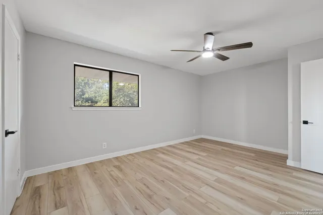an empty room with wooden floor ceiling fan and windows