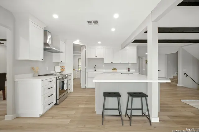 a large white kitchen with kitchen island a sink white cabinets and stainless steel appliances