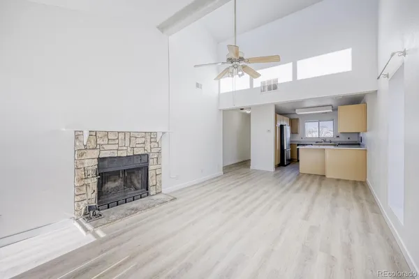 an empty room with wooden floor a fireplace a kitchen island and stainless steel appliances