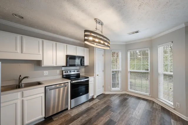 a kitchen with granite countertop a stove top oven a sink dishwasher a refrigerator and white cabinets with wooden floor