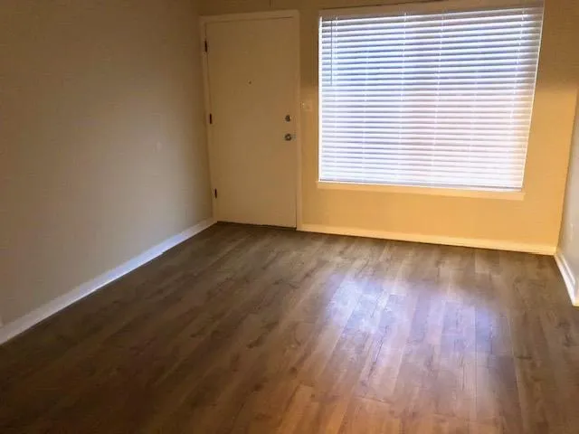 a view of an empty room with wooden floor and a window