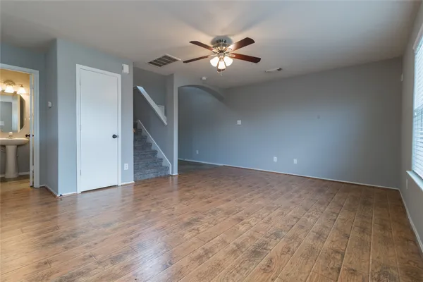 a view of an empty room with wooden floor and a ceiling fan
