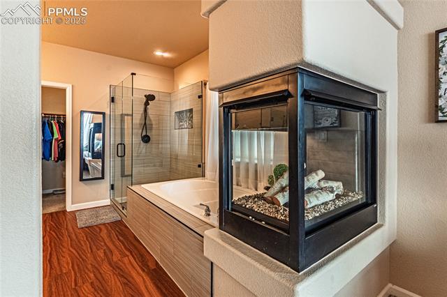 13812 Windy Oaks Road Colorado Springs, CO 80921 - Photo 24 of 50 Bathroom featuring a shower stall, wood finished floors, a walk in closet, a bath, and baseboards