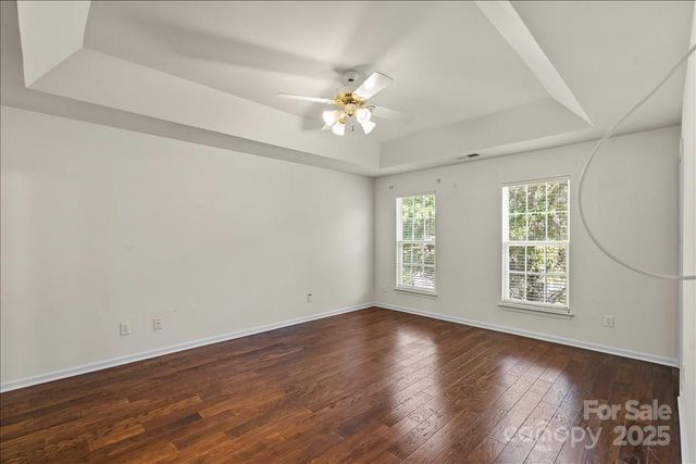 an empty room with wooden floor chandelier fan and windows