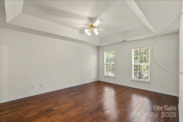 an empty room with wooden floor chandelier fan and windows