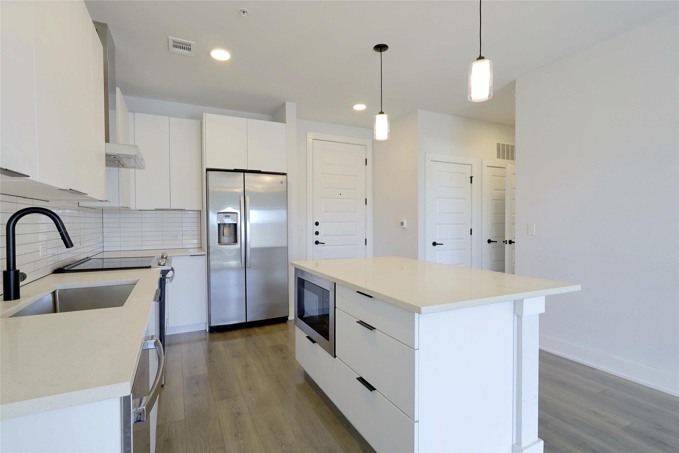 2220 Webberville Road, Unit 303 Austin, TX 78702 - Photo 7 of 14 Kitchen featuring white cabinets, stainless steel appliances, modern cabinets, dark wood finished floors, and hanging light fixtures
