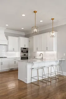a kitchen with granite countertop a stove a sink and white cabinets with wooden floor
