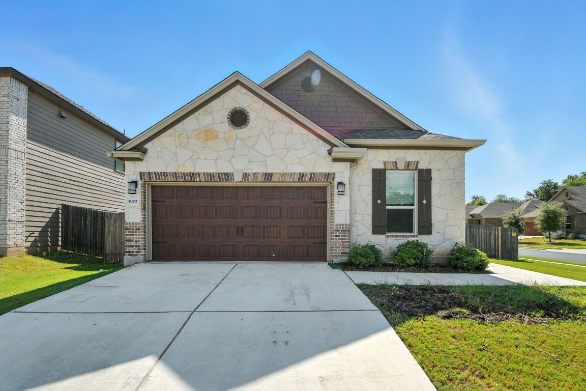 View of front of home featuring an attached garage, concrete driveway, and stone siding