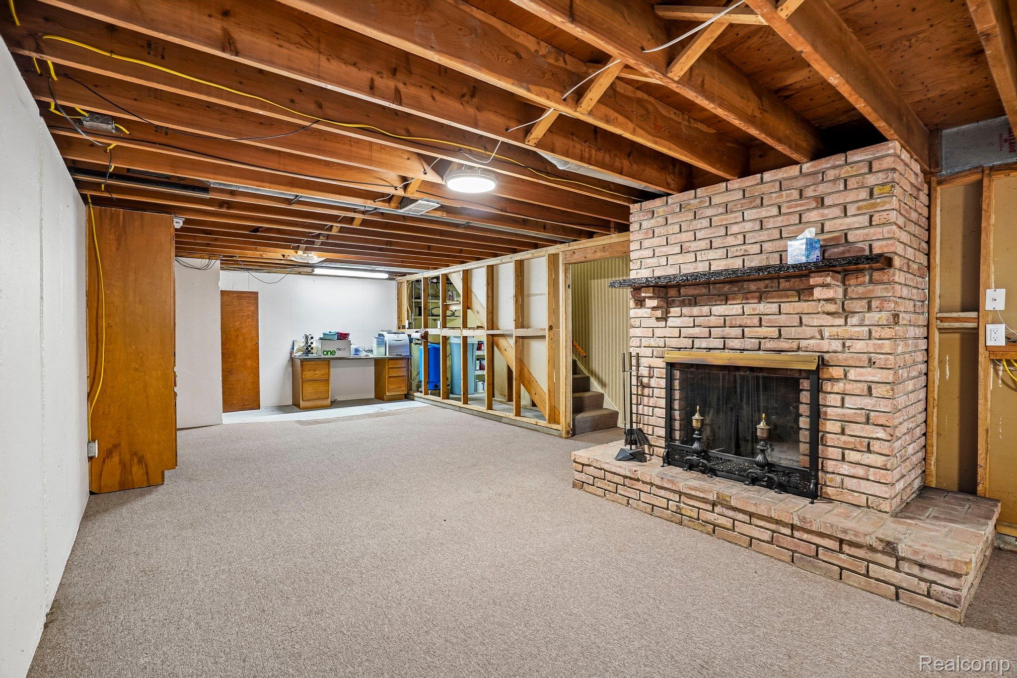 3981 South State Road Durand, MI 48429 - Photo 21 of 33 Exposed wood beam ceiling, brick fireplace with mantel, carpeted flooring, and built-in desk area