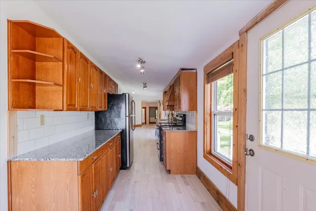 a kitchen with stainless steel appliances granite countertop a refrigerator a sink dishwasher a stove and a dining table with wooden floor