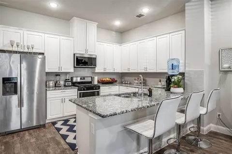 a kitchen with stainless steel appliances granite countertop a stove a sink a microwave a refrigerator and white cabinets