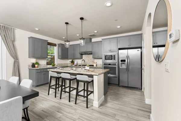 a kitchen with stainless steel appliances kitchen island granite countertop a refrigerator a stove a sink a dining table and chairs with wooden floor