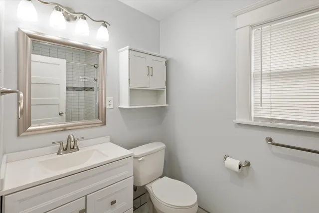 a bathroom with a granite countertop toilet a sink a mirror and a window
