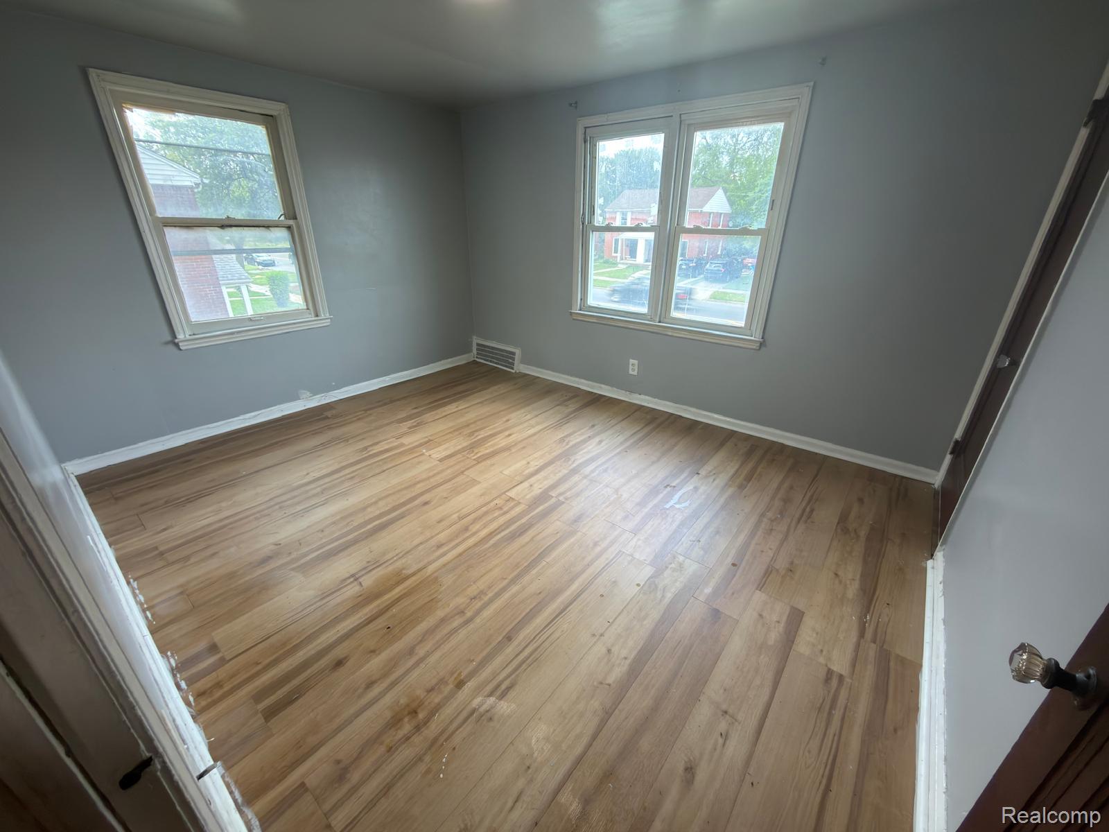 8837 Evergreen Road Detroit, MI 48228 - Photo 14 of 16 Spacious room featuring light wood-finish flooring, two windows with white trim, gray wall paint, white baseboards, and a floor vent