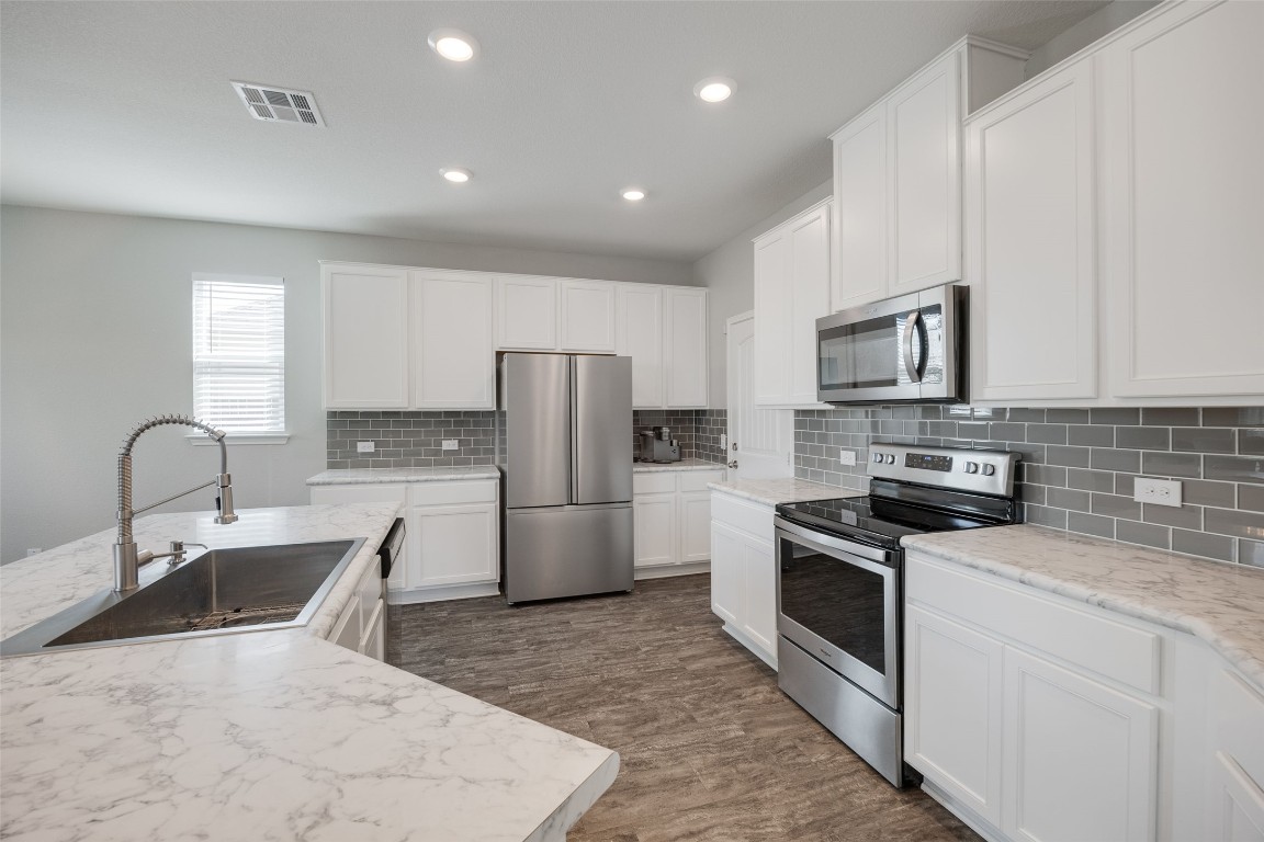 214 Saranac Drive Elgin, TX 78621 - Photo 8 of 37 a kitchen with stainless steel appliances granite countertop a sink a stove a refrigerator with white cabinets and wooden floor