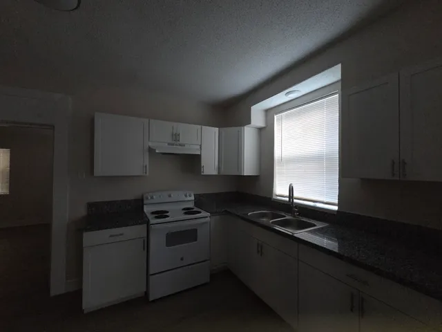 a kitchen with granite countertop a sink a stove and cabinets