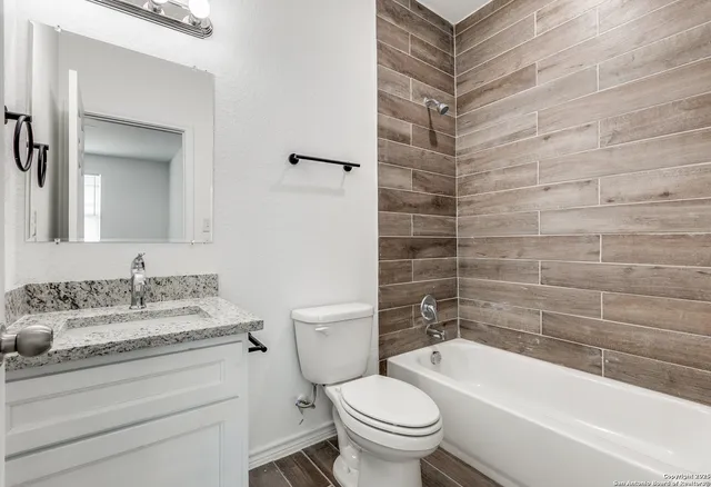 a bathroom with a granite countertop bathtub shower sink mirror vanity and toilet