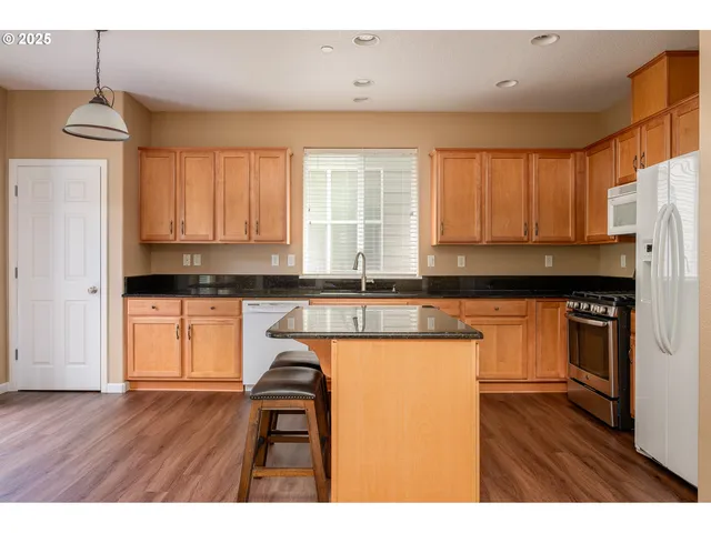 a kitchen with stainless steel appliances granite countertop a refrigerator a sink dishwasher a stove and white countertops with wooden floor