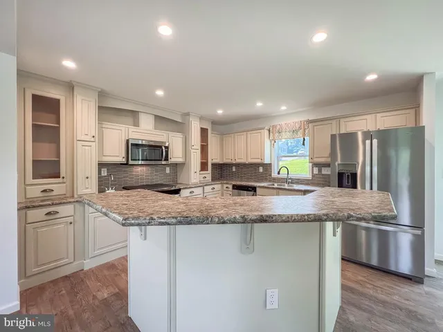 a large kitchen with stainless steel appliances granite countertop a stove a sink a refrigerator and white cabinets with wooden floor