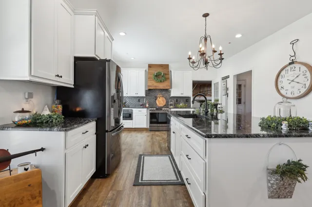 a kitchen with stainless steel appliances granite countertop a refrigerator a stove a sink dishwasher and white cabinets with wooden floor