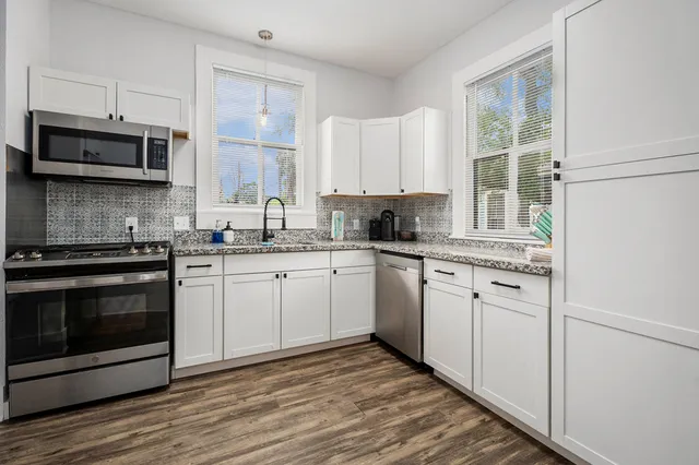 a kitchen with granite countertop white cabinets stainless steel appliances and a window