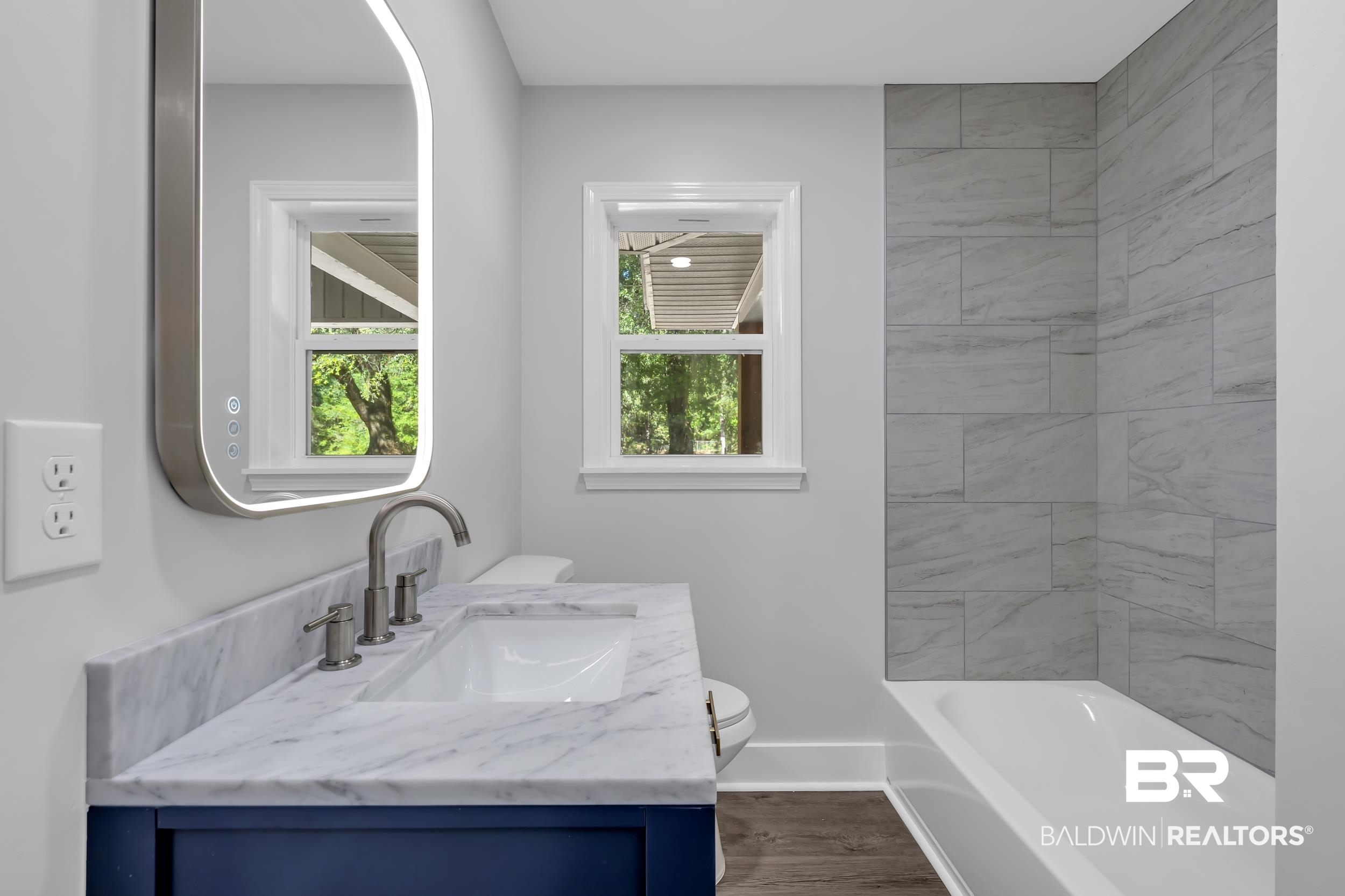 2712 Shelton Beach Rd Extension Mobile, AL 36613 - Photo 19 of 24 Bathroom featuring a built-in bathtub with light gray tiled surround, wood-finish flooring, and a window with white trim