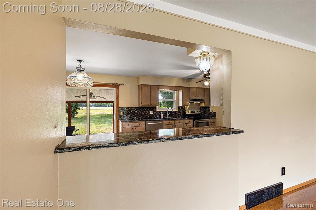 15250 34 Mile Road Armada, MI 48005 - Photo 24 of 49 Kitchen pass-through with a stone countertop, wood-finish cabinetry, mosaic tile backsplash, and stainless steel appliances