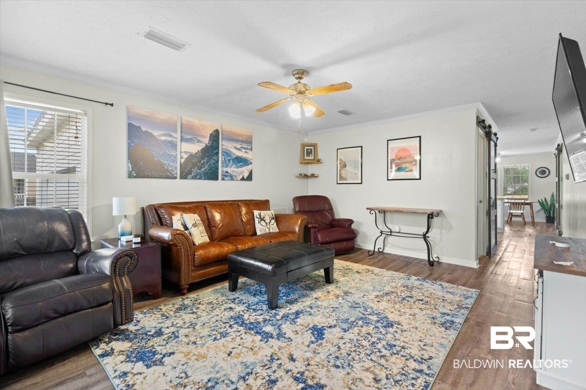 6971 March Road Theodore, AL 36582 - Photo 5 of 26 Living area featuring visible vents, crown molding, baseboards, wood finished floors, and a ceiling fan