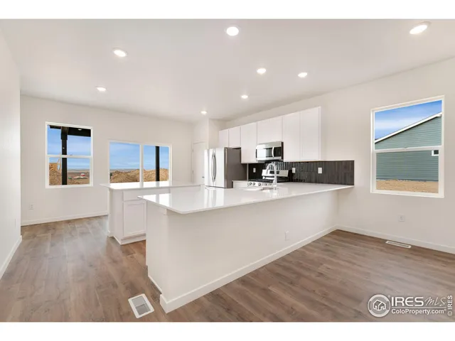 a living room with stainless steel appliances kitchen island granite countertop a refrigerator a sink a stove and white cabinets with wooden floor