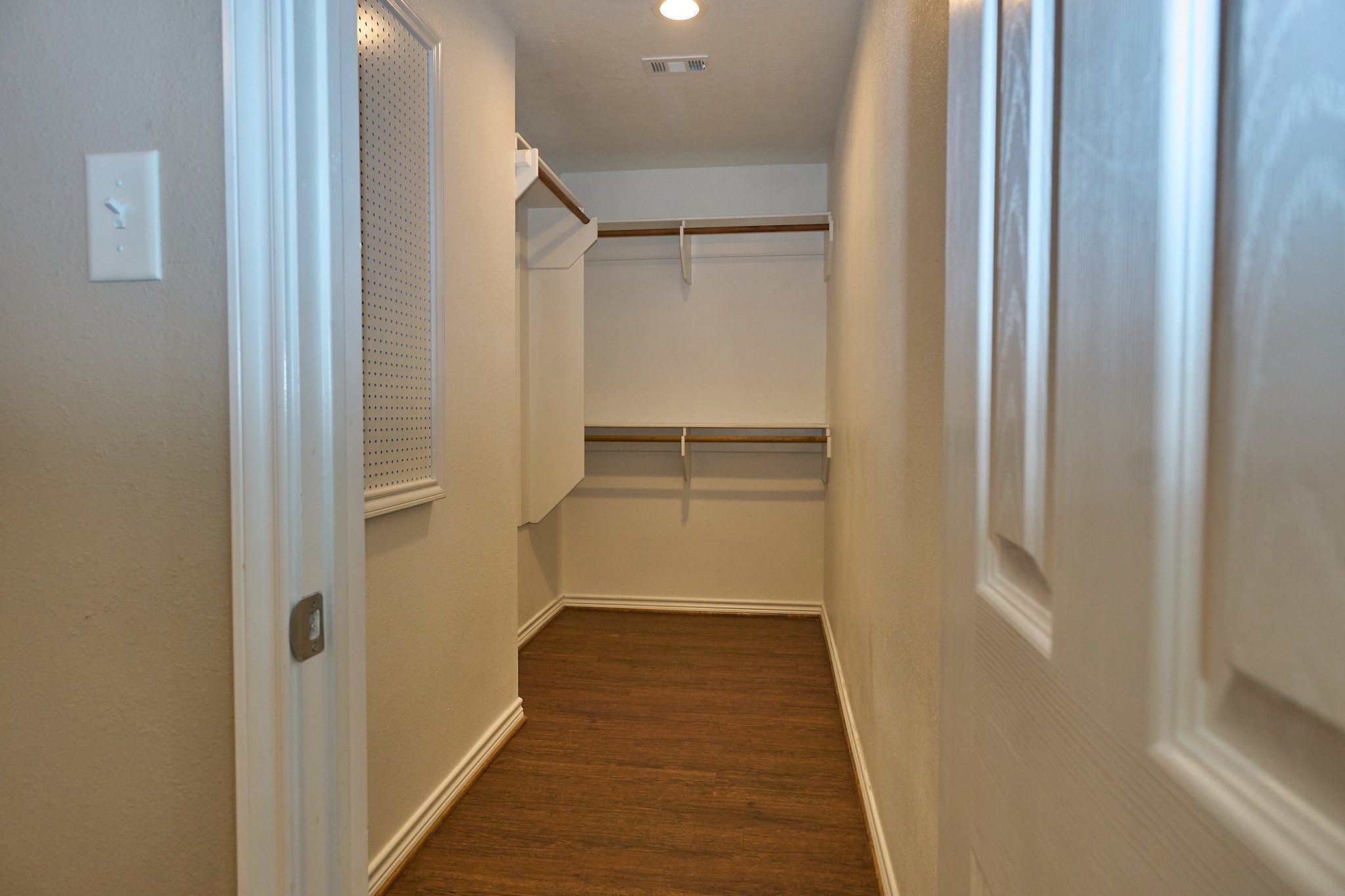 1807 Nuches Lane Bryan, TX 77803 - Photo 14 of 27 This photo showcases a narrow walk-in closet with wooden floors and light-colored walls. It features shelving and hanging rods, providing ample storage space. The closet is well-lit and appears to be neatly organized.