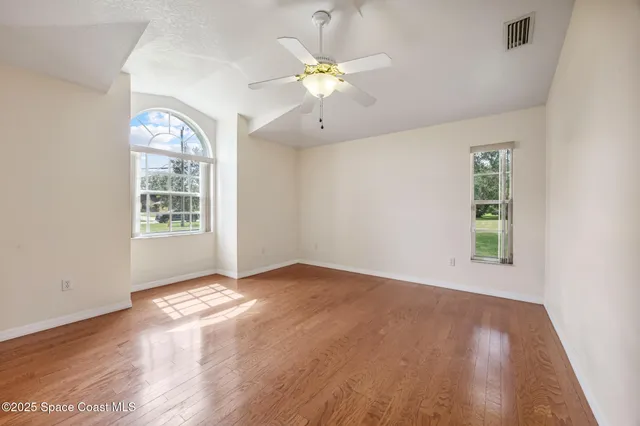 an empty room with wooden floor chandelier fan and windows