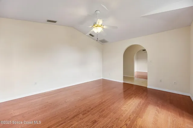 a view of an empty room with wooden floor and a ceiling fan