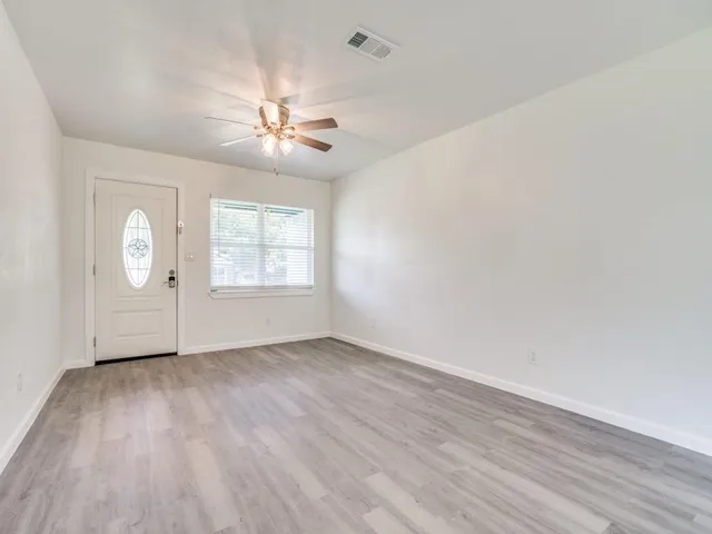 an empty room with wooden floor chandelier fan and windows