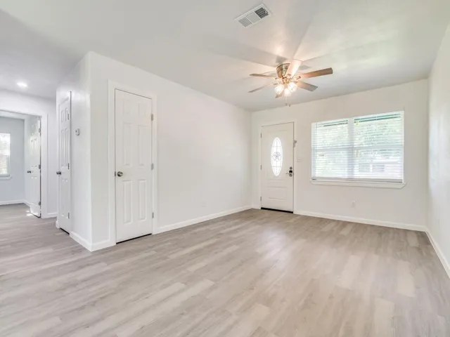 an empty room with wooden floor fan and windows