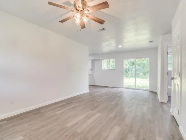 an empty room with wooden floor fan and windows