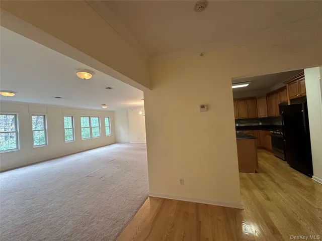 a view of empty room with wooden floor and kitchen