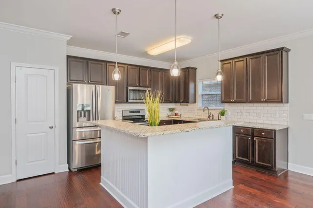 a kitchen with stainless steel appliances granite countertop a refrigerator a sink dishwasher a stove and white cabinets with wooden floor