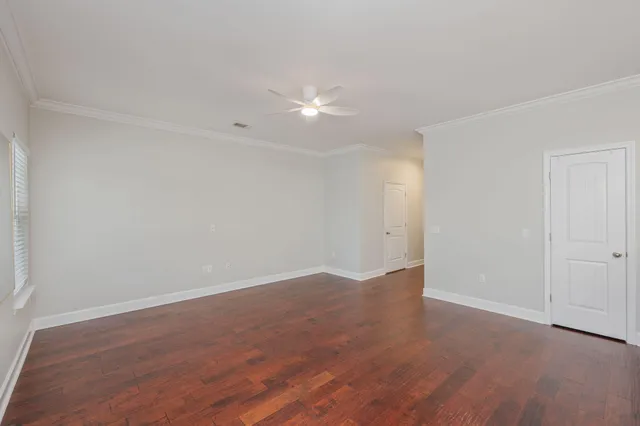a view of an empty room with wooden floor and fan
