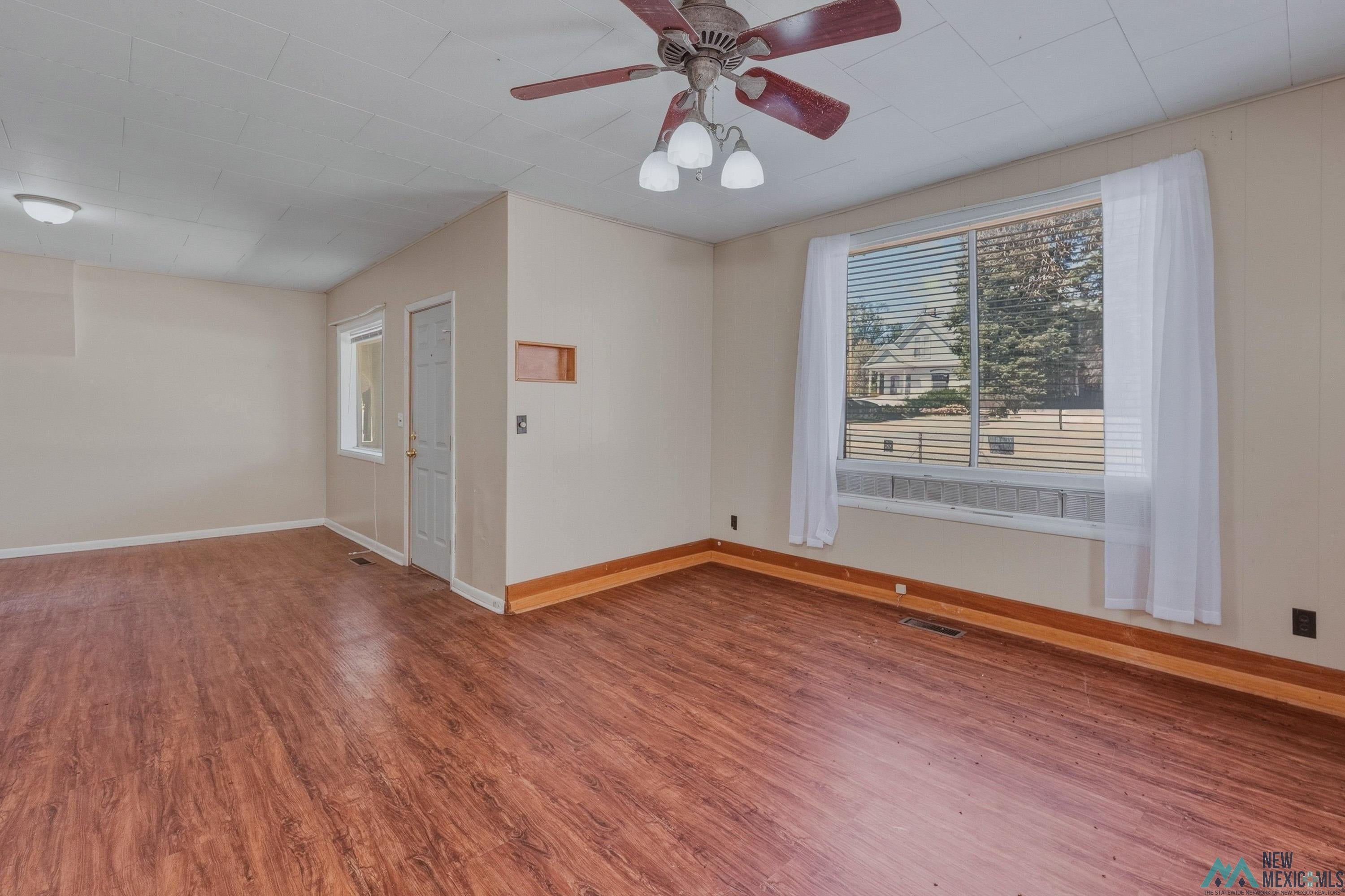 533 South 2nd Street Raton, NM 87740 - Photo 7 of 43 Spacious room featuring wood-finish flooring, a ceiling fan with integrated lighting, and a large window with blinds