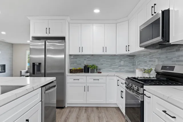 a kitchen with stainless steel appliances granite countertop a refrigerator a sink dishwasher and white cabinets with wooden floor