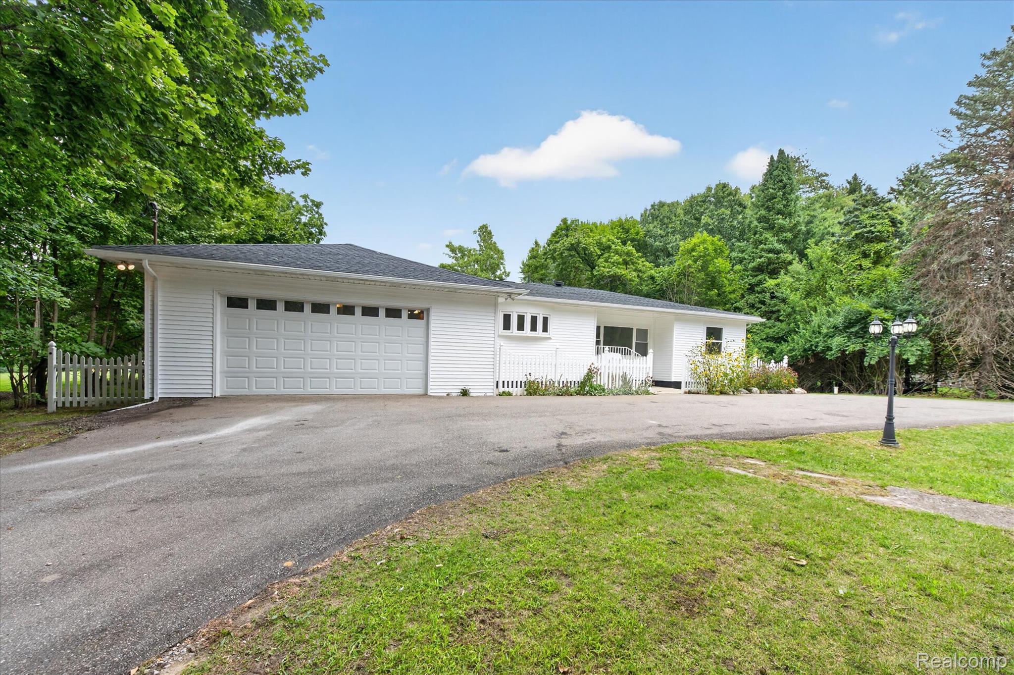 White siding exterior with a multi-car garage, asphalt driveway, and a white picket fence