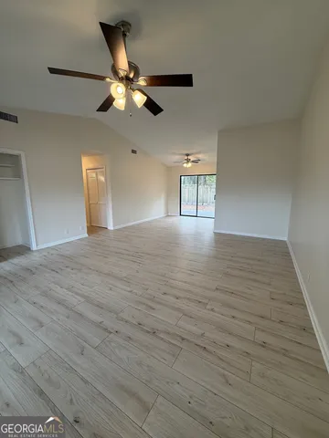 a view of an empty room with wooden floor and a ceiling fan