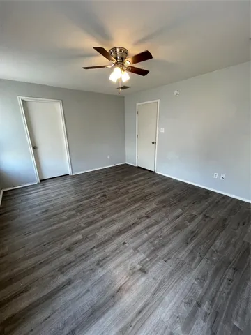 a view of an empty room with wooden floor and a ceiling fan