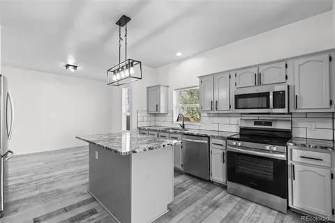 a kitchen with stainless steel appliances a stove top oven a sink dishwasher a refrigerator and a dining table with wooden floor