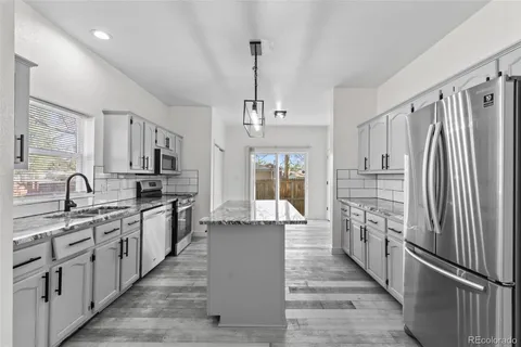 a kitchen with stainless steel appliances granite countertop a refrigerator a sink dishwasher a oven with white cabinets and wooden floor