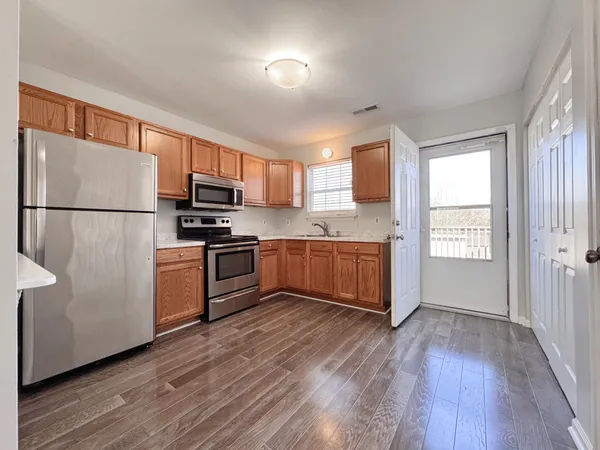a kitchen with granite countertop a refrigerator a stove top oven and wooden floors