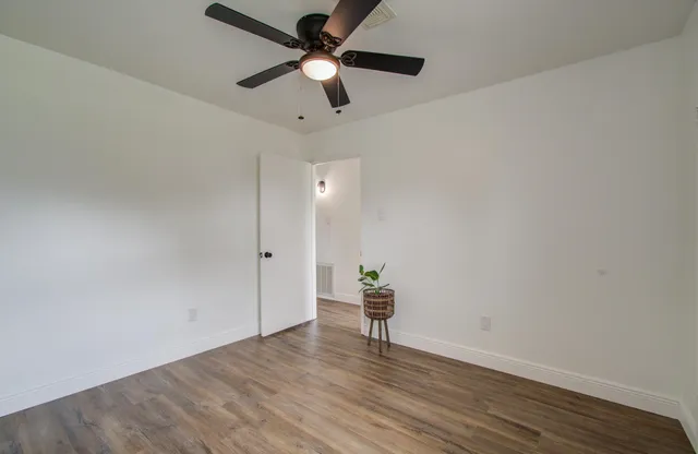 an empty room with wooden floor chandelier fan and windows