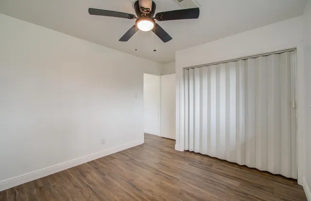 an empty room with wooden floor fan and windows