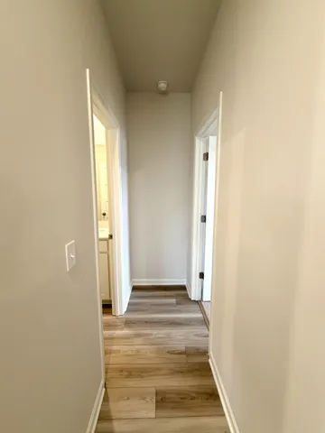 a view of a hallway with wooden floor and a bathroom